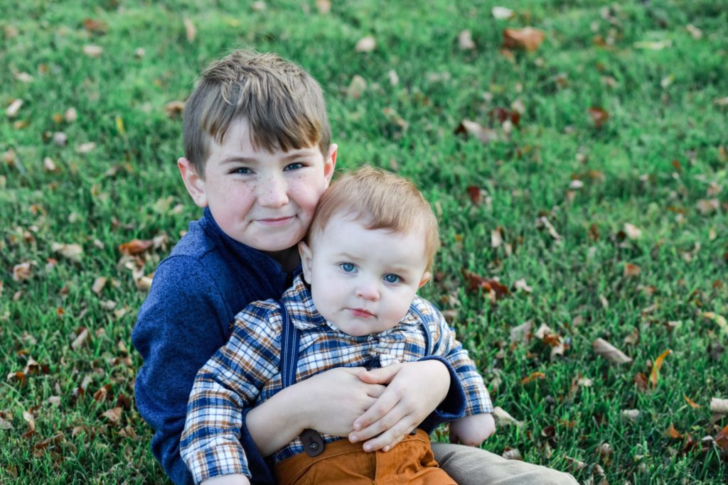 brothers.Big brother holding little brother on his lap sitting pn the grass