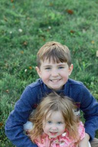 big brother sitting in the grass holding his little sister