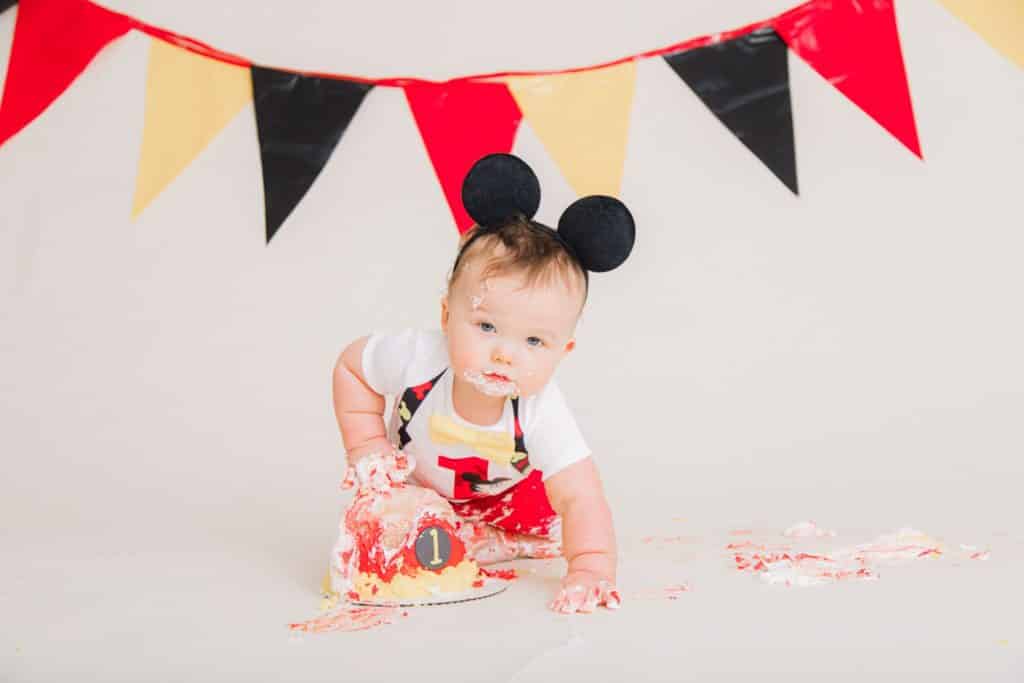 red, yellow, black banner with one year boy, mickey mouse ears, red one on his shirt with a mickey mouse cake