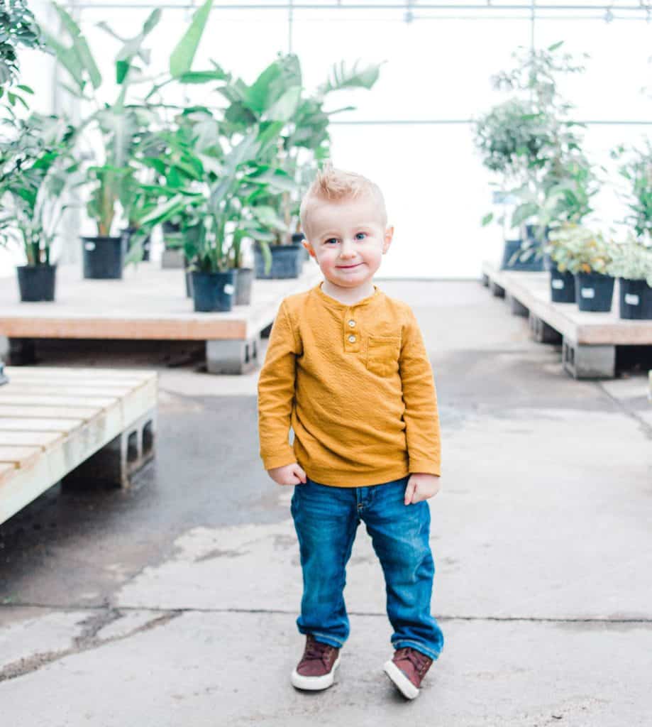 Maine toddler standing in greenhouse looking at the camera