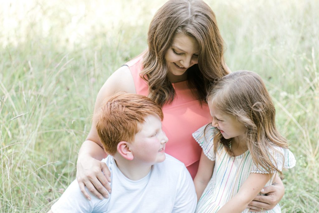 mother and two kids sitting in tall grass, mother looking down at her kids 