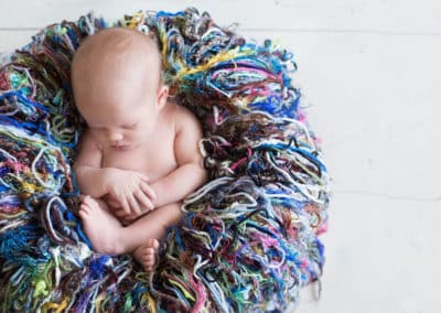 brunswick maine newborn photographer gets a shot of a newborn baby sleeping curled up in a colorful basket