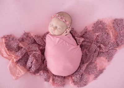 newborn wrapped in blanket with pink background